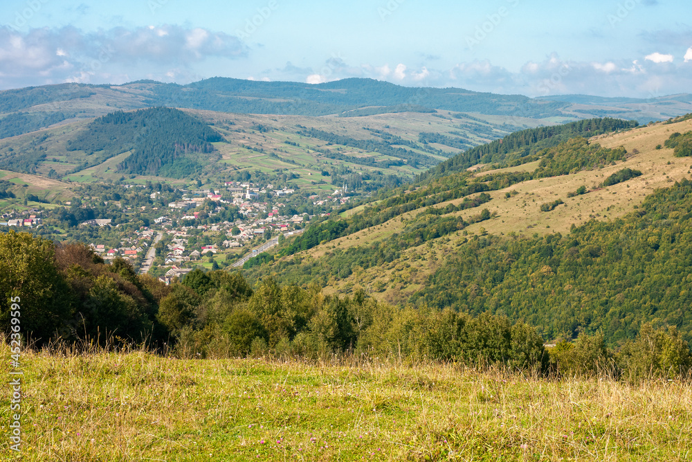 carpathian countryside in september. beautiful mountain landscape with grassy field on the hill. rural scenery with village in the distant valley on a sunny day with clouds on the sky