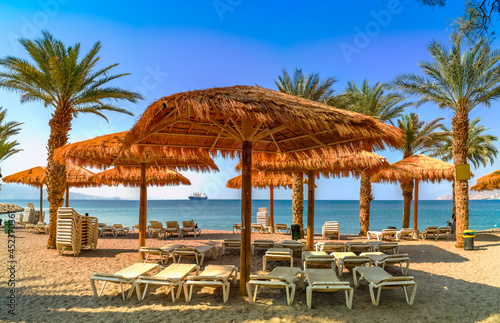 Morning on sandy beach of the Red Sea in Eilat - famous tourist resort city in Israel  at the distance seen ocean cargo ship going to the marine port of Eilat
