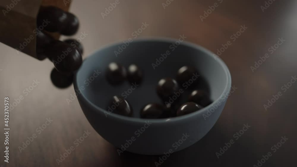 Slow motion chocolate covered hazelnuts pour into blue bowl on walnut table Slow motion chocolate covered hazelnuts pour into blue bowl on walnut table