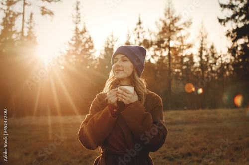 Foto Young woman with cup of coffee stay near wood in sunset time