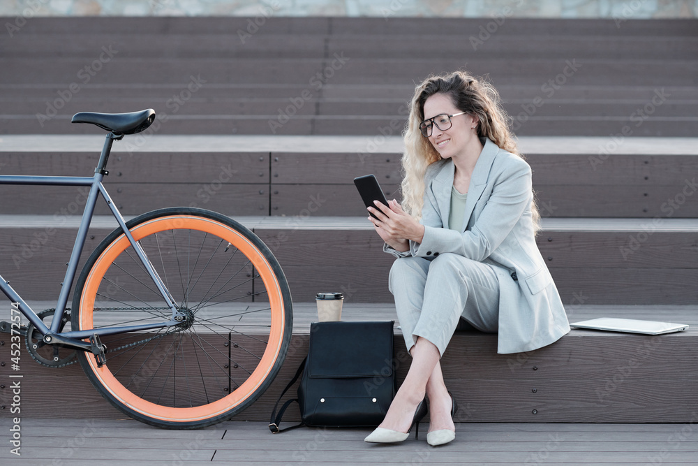 Happy businesswoman looking at smartphone screen while having break in urban environment Happy businesswoman looking at smartphone screen while having break in urban environment