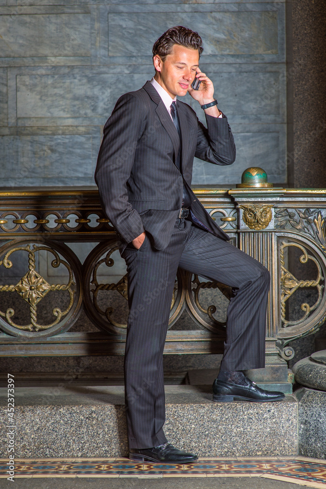 Dressing formally and standing by a railing a young businessman is smilingly talking on a mobile phone.. Dressing formally and standing by a railing a young businessman is smilingly talking on a mobile phone..
