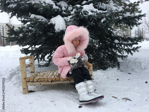 Wallpaper Mural a girl in a pink jacket is sitting  on a bed under a christmas tree in the snow and waiting. its cold outside and the branches of the fir tree are in the frame.a glance to the side Torontodigital.ca