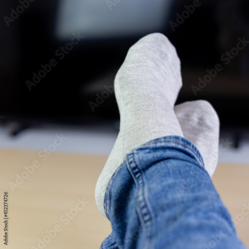 Relaxing woman laying in sofa front of TV, holding her legs on table