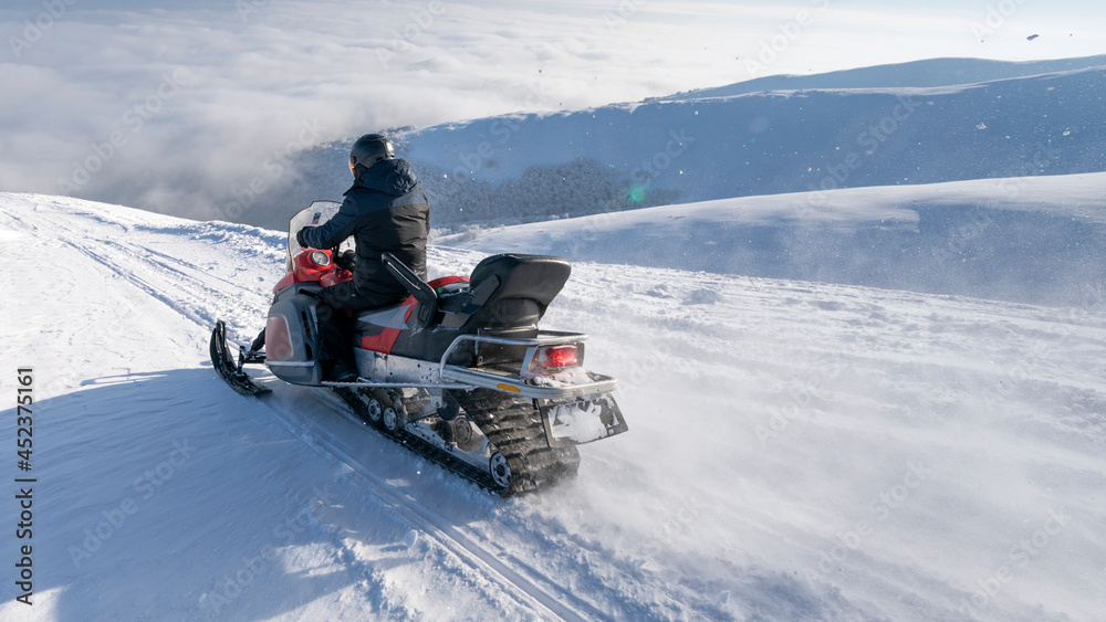 The snowmobile moves on the slope of a snow-capped mountain.