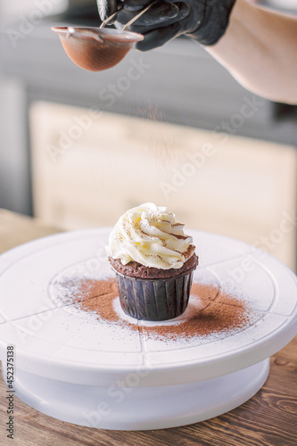 The girl sprinkles cocoa on the cupcakes through a sieve