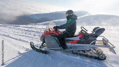 The snowmobile moves on the slope of a snow-capped mountain.