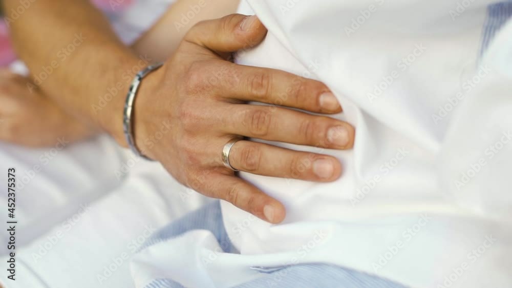 A man with a hand with a silver wedding ring and a bracelet gently strokes his wife's belly in which their loving long-awaited baby grows. Happy family expecting a newborn A man with a hand with a silver wedding ring and a bracelet gently strokes his wife's belly in which their loving long-awaited baby grows. Happy family expecting a newborn