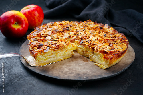 Traditional apple pie torta di mele cremosa with almond flakes served as close-up on a rustic design plate at a black board photo