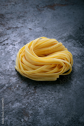 Classic Fresh raw tagliolini pasta rolled with a nest on a stone background. Type of Italian pasta