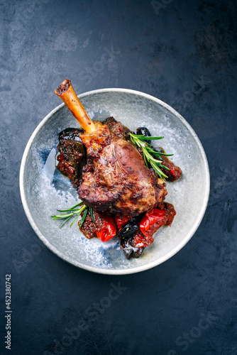 Modern style traditional braised slow cooked lamb shank in red wine sauce with eggplants and tomatoes served as top view in a design bowl photo