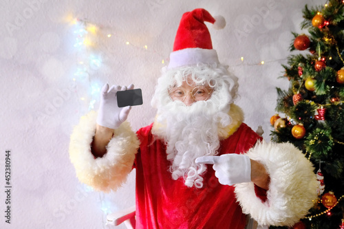 elderly santa claus in a suit, with a white beard congratulates children and adults, holds a blank credit card in his hand, concept of christmas, holiday discounts, shopping, gifts