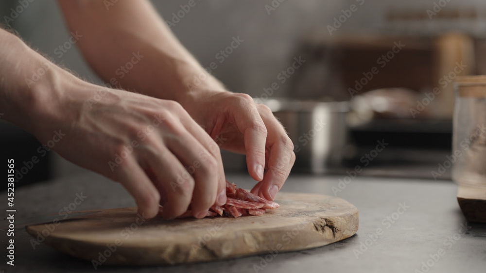 man arrange choped salami on olive board