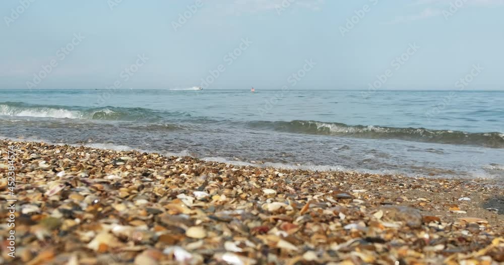 Sea waves come ashore with small stones and shells, a man swims in the background and a water scooter rides on the water. Sea waves come ashore with small stones and shells, a man swims in the background and a water scooter rides on the water.
