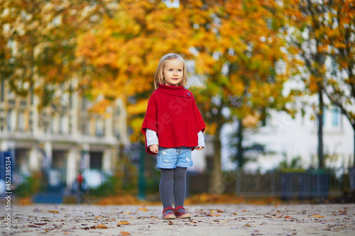 Adorable little girl in red poncho walking in autumn park on a sunny fall day. © Ekaterina Pokrovsky