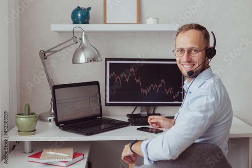 Successful smiling man in headset trades on stock market, technical support. Technical charts on displays photo