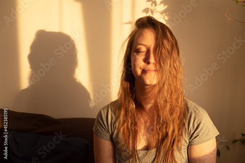 Young woman close eyes and relaxation in warm rays of sunset. Warm calm portrait of girl indoor