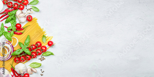 pasta, cherry tomato, onion, garlic, peppercorns, chili peppers and basil on a gray table