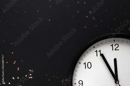 New Year's white black clock, five minutes to midnight on a dark black background with gold stars and blank space for text. Merry Christmas. Christmas holiday.