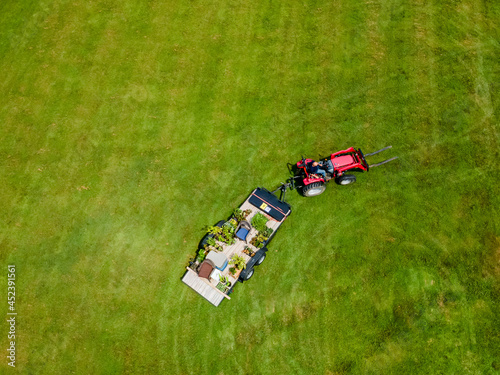 A red tractor pulls a trailor with plants on it through a green grass field on a sunny clear summer day.  Aerial perspective looking down as the photograph was shot from an drone. photo