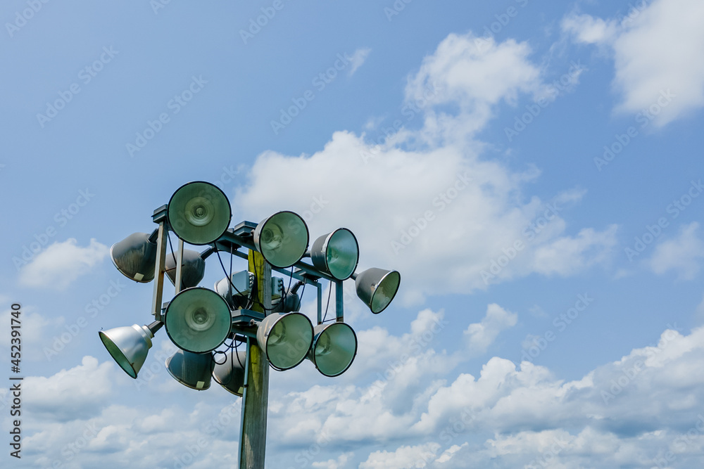 Metal sport stadium lights on a wooden pole contrasted against a blue sky with cumulus clouds during a sunny summer day. Metal sport stadium lights on a wooden pole contrasted against a blue sky with cumulus clouds during a sunny summer day.