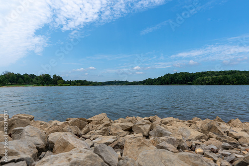 Fototapeta Naklejka Na Ścianę i Meble -  Gorgeous sunny summer day at Freeman Lake in Elizabethtown, KY.  Composed with rocks in the foreground and a blue sky with some clouds in the sky.