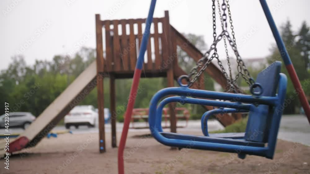 raining on playground. close-up. Empty wet swing swaying in wind, on empty playground, in the yard, during heavy rain