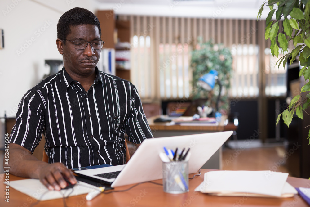Obraz premium Focused african american man working for a large company types documentation on a computer while sitting at workplace ..in the office