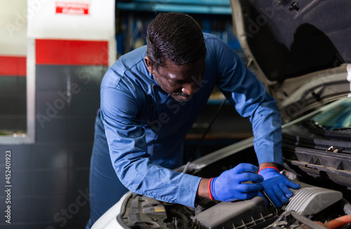 Afro american car mechanic looking at open hood for internal checking of vehicle in workshop