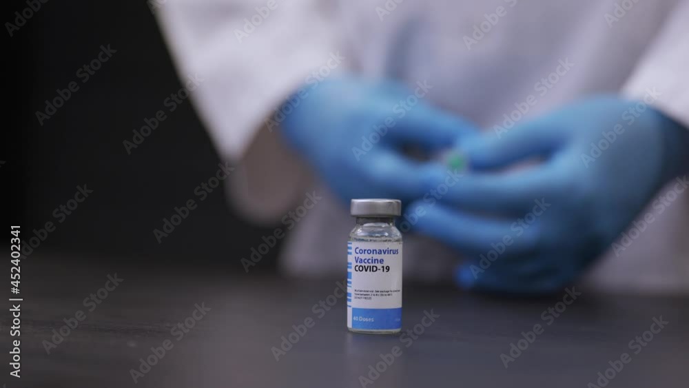 Vial of Covid 19 Vaccine On Table With Doctor In Background and Syringe In Hands Vial of Covid 19 Vaccine On Table With Doctor In Background and Syringe In Hands