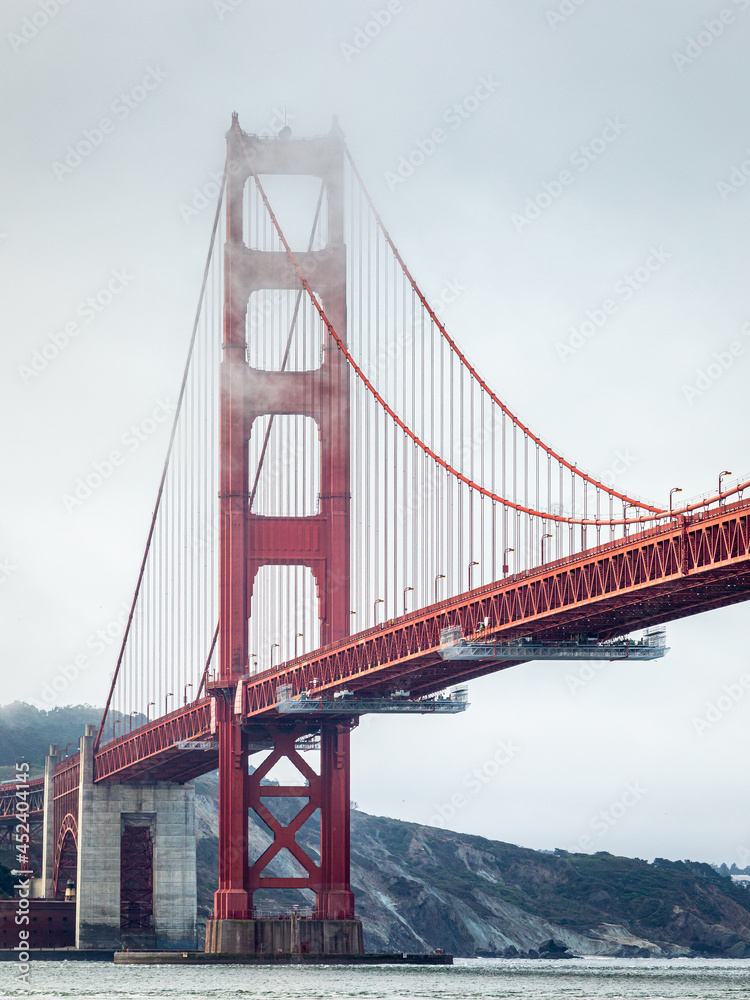 Golden gate bridge covered by fog at overcast sunrise.