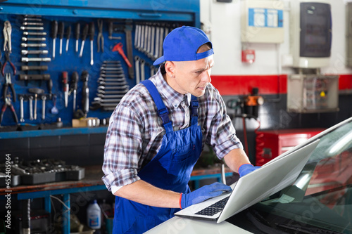 Mechanic man with laptop making car diagnostics at auto service photo