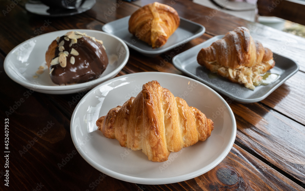 Various flavors of fresh baked croissants served with plate on wooden table. Croissant is a French buttery, flaky and crescent-shaped bread. Various flavors of fresh baked croissants served with plate on wooden table. Croissant is a French buttery, flaky and crescent-shaped bread.