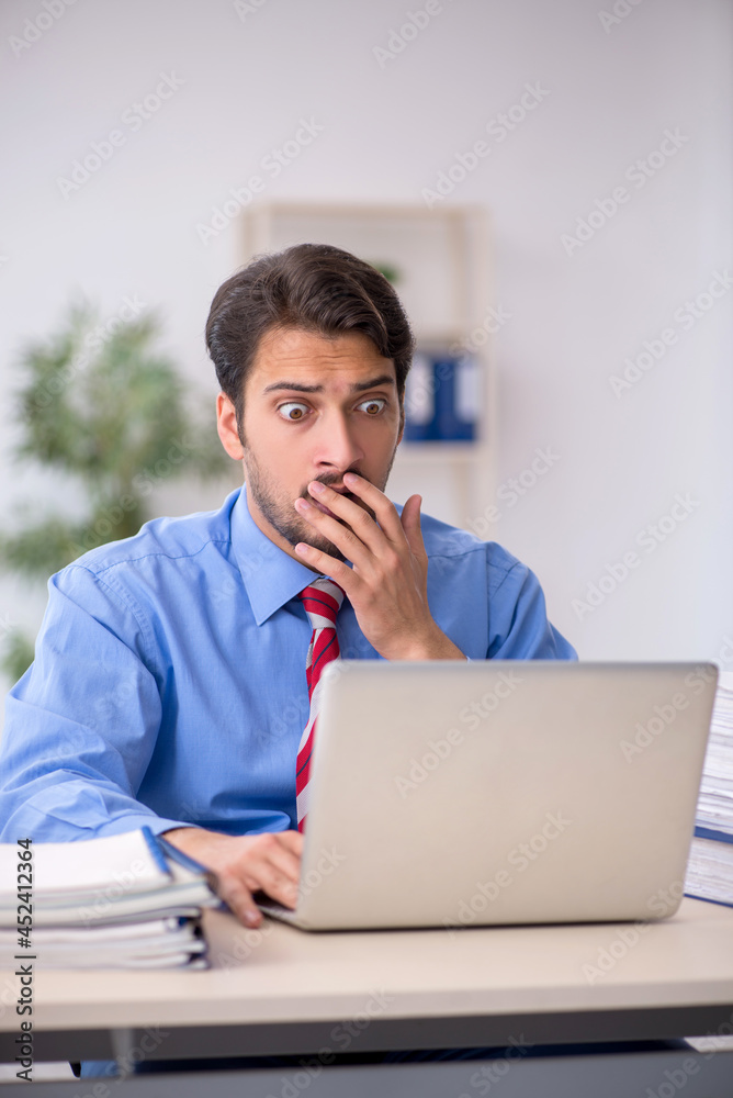 Young male employee unhappy with excessive work in the office Young male employee unhappy with excessive work in the office