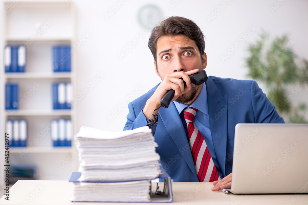 Fototapeta premium Young male employee unhappy with excessive work in the office