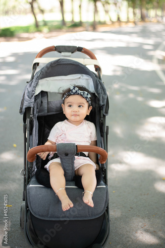 full body image of happy Asian baby sitting in a stroller Blurred background of a shady public garden