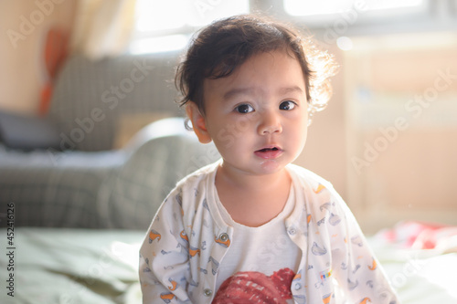 Portrait of a cute happy little Asian baby girl she sit on bed and look at camera, baby expression concept