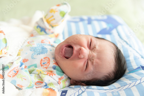 Top view of cute little Asian baby girl lying on bed and crying