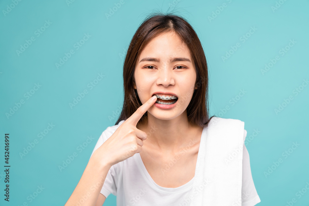 Woman wearing braces with sensitive teeth and hands touch the cheeks on blue background, Concept oral hygiene and health care. Woman wearing braces with sensitive teeth and hands touch the cheeks on blue background, Concept oral hygiene and health care.