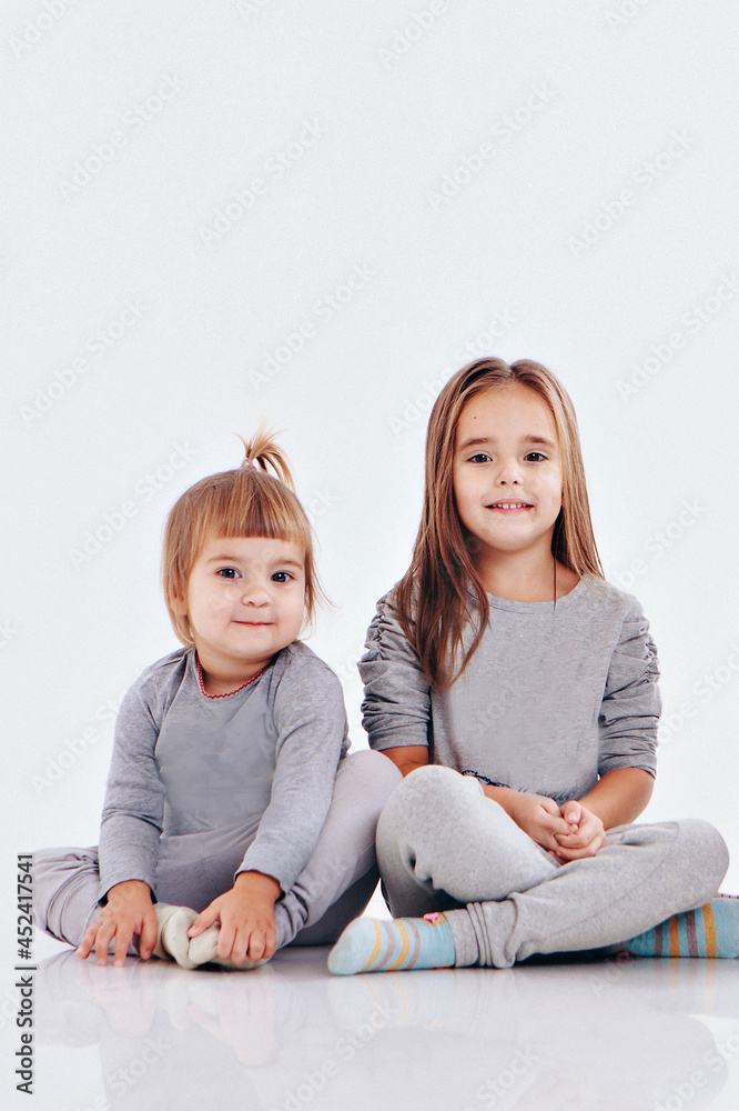 Couple of twins sitting on the floor isolated on a white background. Children in gray clothes Couple of twins sitting on the floor isolated on a white background. Children in gray clothes