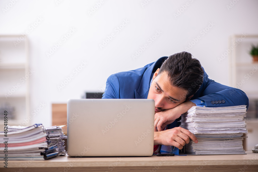 Young male employee unhappy with excessive work at workplace Young male employee unhappy with excessive work at workplace