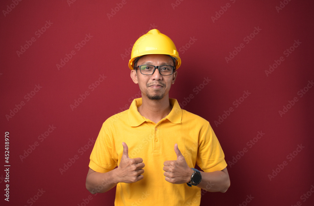 Handsome Asian worker man wearing helmet smiling and thumbs up over isolated red background. Handsome Asian worker man wearing helmet smiling and thumbs up over isolated red background.