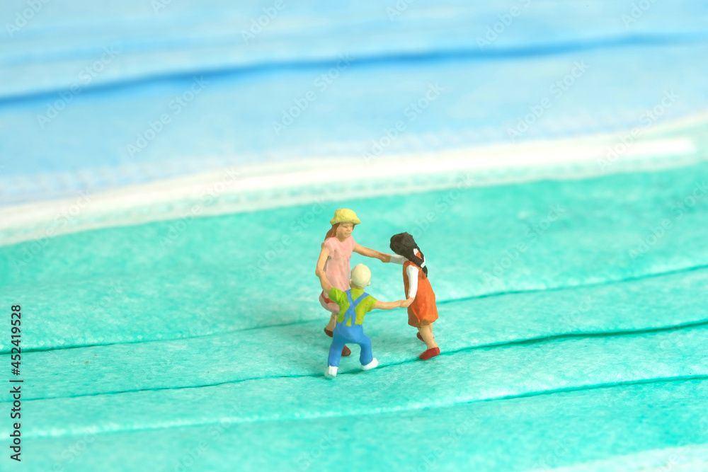 Miniature people toy figure photography. Playing on pandemic concept. A group of kids playing above surgical face mask, isolated on white background.