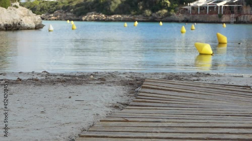 Cala Santandria in Menorca: sand, wooden path, navigation lane of yellow buoys indicating the way for boats, Balearic Islands, Spain. photo