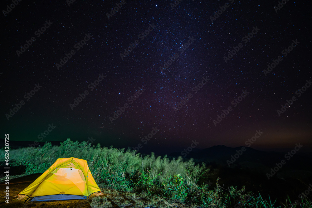 Tourist tent in camp among meadow with Panorama view universe space shot of milky way galaxy with stars on night sky background at mountains landscape Thailand