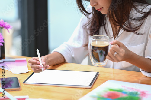 Cropped shot creative woman drinking coffee and drawing picture on digital tablet.