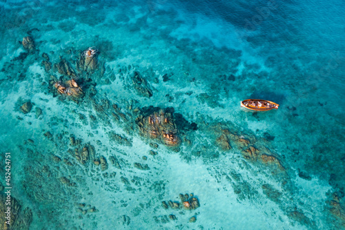 View from above, stunning aerial view of a wooden boat anchored to some rocks bathed by a crystal clear, turquoise water. Giardinelli island, La Maddalena Archipelago, Sardinia, Italy.