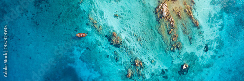 View from above  stunning aerial view of a wooden boat anchored to some rocks bathed by a crystal clear  turquoise water. Giardinelli island  La Maddalena Archipelago  Sardinia  Italy.