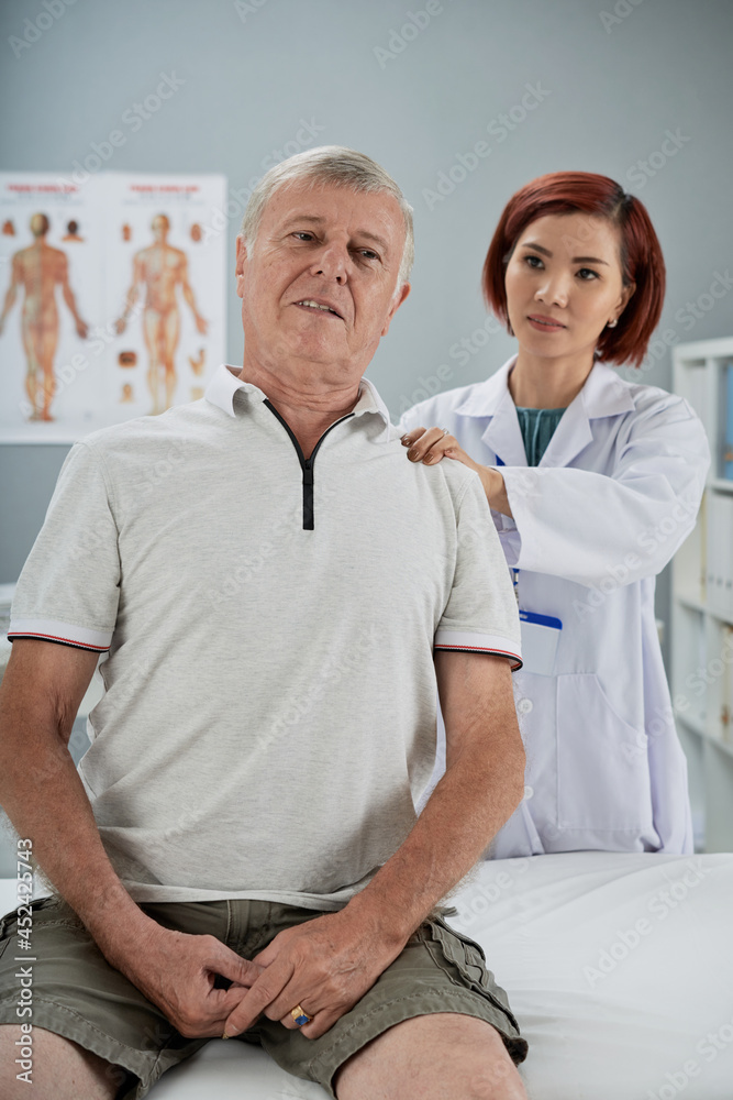 Obraz premium Physiotherapist examining senior patient, she is massaging various trigger points on his back and askig if it is painful