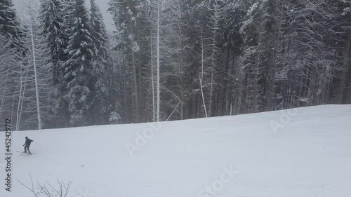A skier and a snowboarder going downhill on the snowy winter slope of Bukovel ski resort in the Ukrainian Carpathian mountains. 